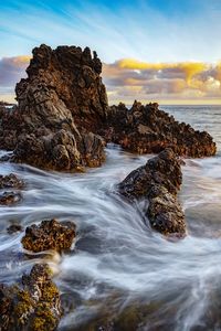 Rocks in sea against sky during sunset