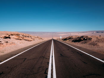Road leading towards desert against clear blue sky