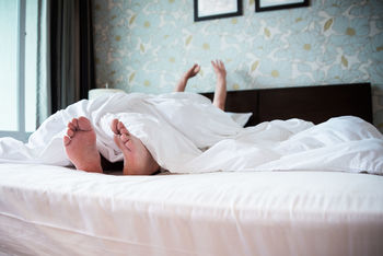 Person relaxing under blanket on bed at home