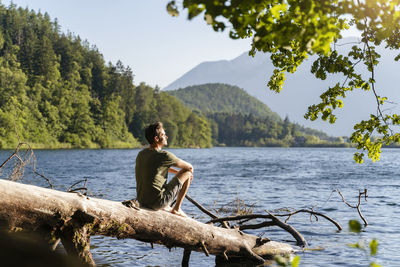 Man looking at view while siting on fallen tree at lake