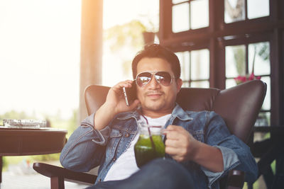 Young man using smart phone while holding juice at cafe