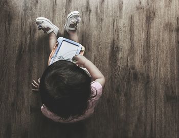 High angle view of girl with slate sitting on hardwood floor at home