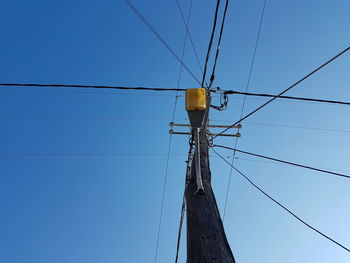 Low angle view of electricity pylon against clear blue sky