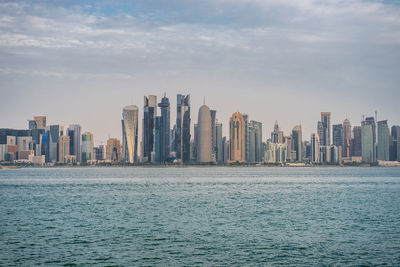 Sea by modern buildings against sky in city