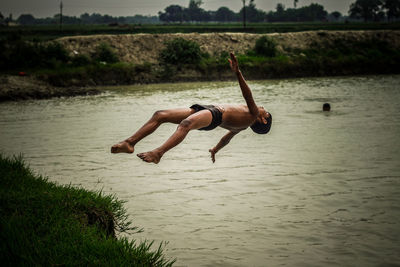 Side view of young man jumping in lake