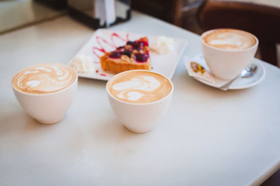 High angle view of pastry with cappuccinos served on table