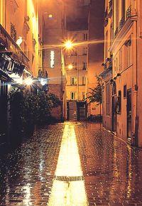 Illuminated street amidst buildings against sky at night