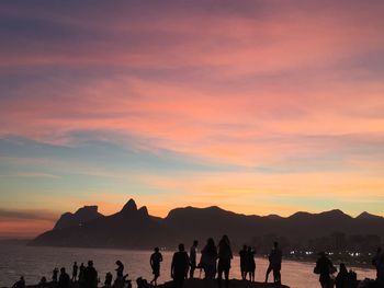 Silhouette people by sea against sky during sunset