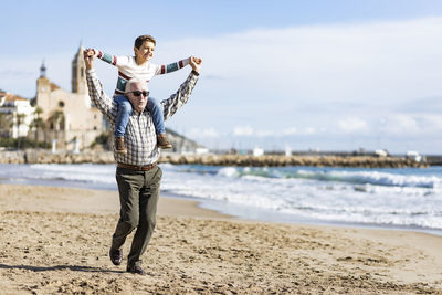 Grandfather carrying grandson on shoulders while walking at beach