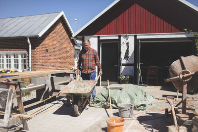 Senior man pushing wheelbarrow at yard outside house