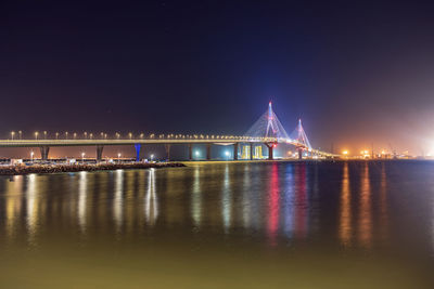 Illuminated bridge over river against sky at night