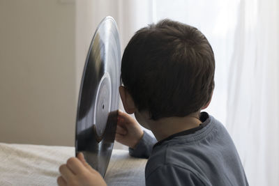 Side view of boy holding turntable on table while sitting at home