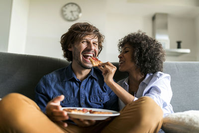 Happy couple sitting on couch eating pizza