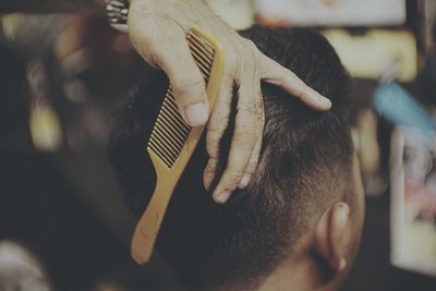 Cropped hand of barber cutting man hair at salon