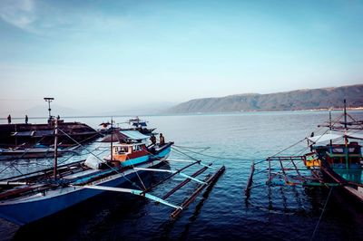 Fishing boats moored on sea against clear sky