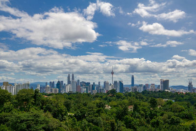 Trees and buildings against cloudy sky during sunny day