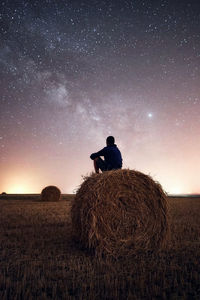 Man sitting on hay bale against sky at night