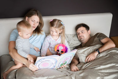 High angle view of parents with children reading book on bed at home