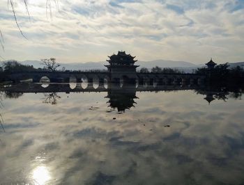 Reflection of bridge in lake against cloudy sky