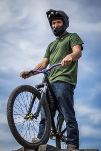 Low angle view of man with bmx cycle standing on ramp against sky