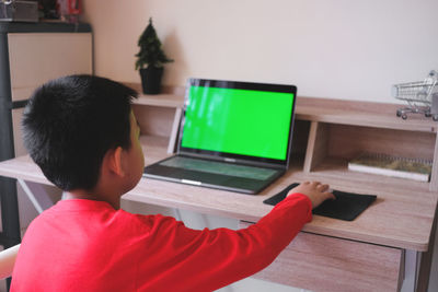 Rear view of boy sitting on table at home