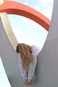 Women leaning on built structure against sky