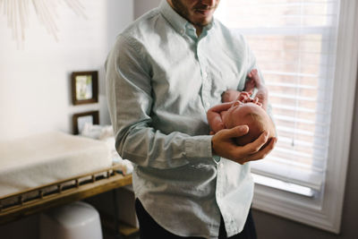 Midsection of father carrying newborn daughter while standing at home