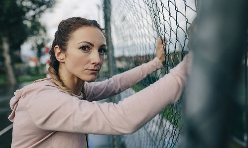 Portrait of young woman standing by fence