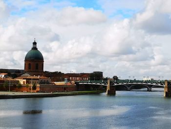 Arch bridge over river amidst buildings against sky