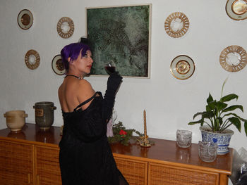 Seductive woman with wine standing against picture frames at home