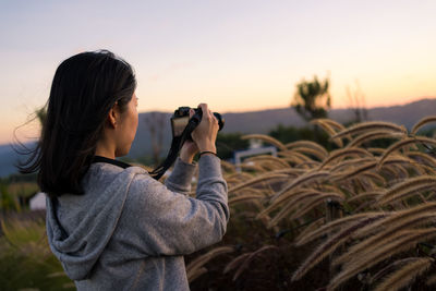 Mature asian woman using camera to shoot photos of flowers at sunset