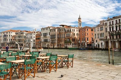 Chairs on walkway by canal and buildings in city