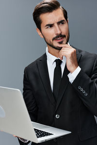 Businessman using laptop while standing against wall