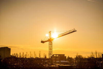 Silhouette cranes at construction site against sky during sunset