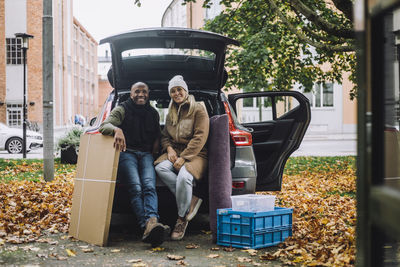 Portrait of smiling mature couple with cardboard box and crate sitting in car during autumn