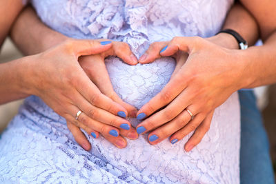 Close-up of couple's hands making heart shape on woman's stomach