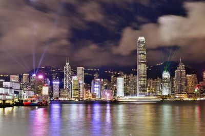 Illuminated city by river against sky at night