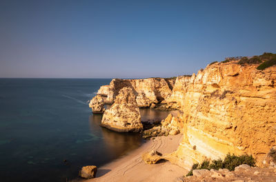 Rock formations by sea against clear sky