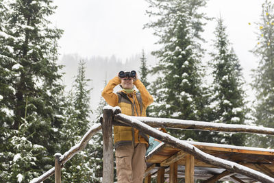 Woman looking through binocular standing near wooden railing