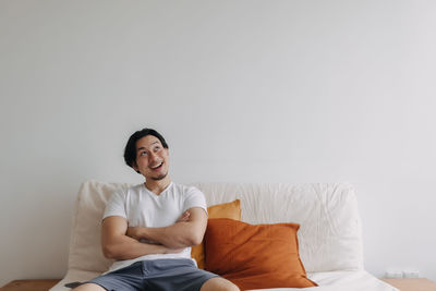 Smiling man looking up while sitting on sofa at home