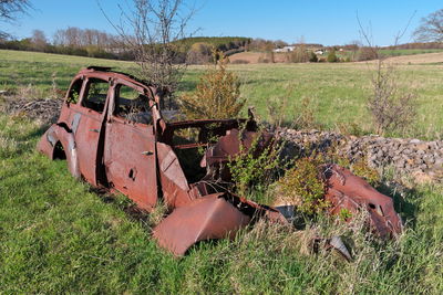 Wide shot of a derelict and rusty antique vintage car abandoned in a farm field on a sunny day. 