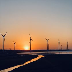 Silhouette wind turbines on land against sky during sunset