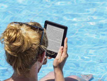 Rear view of woman using digital tablet while sitting at poolside
