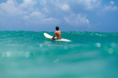 Rear view of man surfing in sea against sky