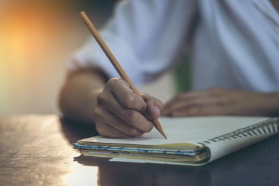 Midsection of woman writing in diary on table