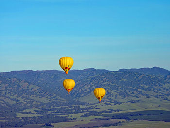 Hot air balloons flying in mountains against clear blue sky