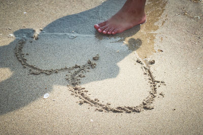 Low section of person standing by heart shape on sand at beach