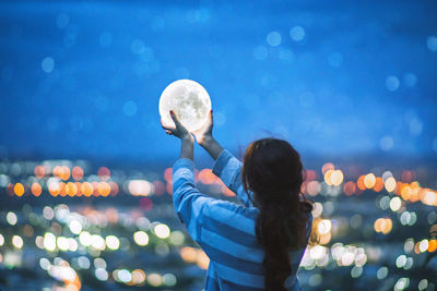 Rear view of woman holding lighting equipment in illuminated city at night