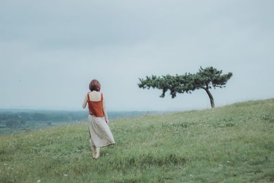 Rear view full length of woman standing on grass against sky