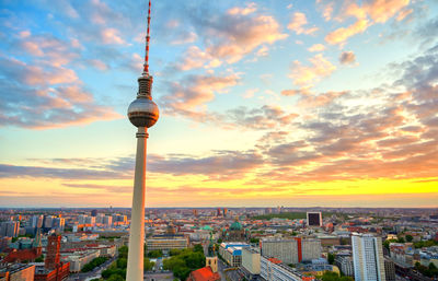 Communications tower in city against sky during sunset